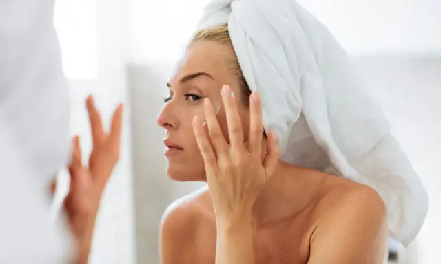Une femme, serviette sur la tête, applique une crème sur son visage. Un geste essentiel pour prendre soin de sa peau en hiver.