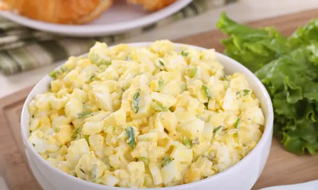 Pyszna sałatka z jajkiem, idealna na śniadanie lub lunch. Podana w białej misce, obok świeżych liści sałaty i chrupiących croissantów.