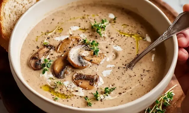 En krämig skål med godaste svampsoppan, toppad med champinjoner, färska örter och en skiva bröd.