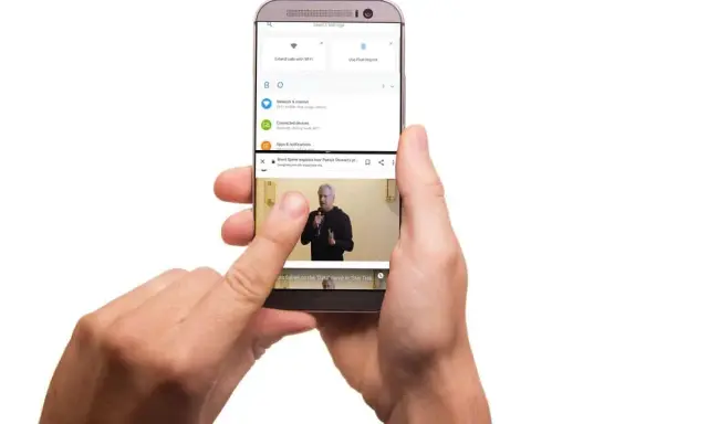 Dwie ręce trzymają telefon, na którym widać, jak podzielić ekran na 2. Górna część pokazuje ustawienia, dolna odtwarza wideo.