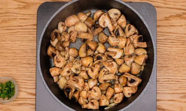 Champiñones al ajillo dorándose en una sartén, con perejil picado en un cuenco al lado.
