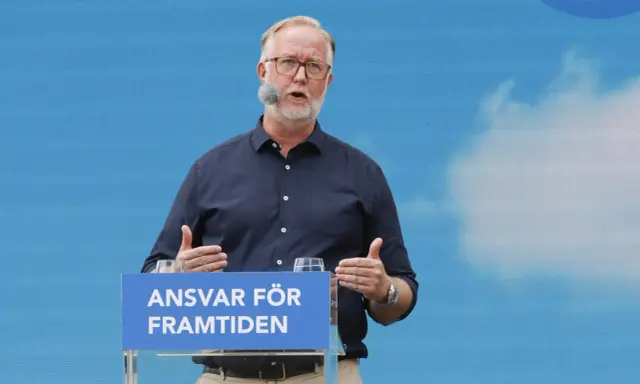 Man med glasögon och mikrofon talar vid ett podium med texten "Ansvar för framtiden". Hans gestik och budskap speglar en liberalism ideologi.