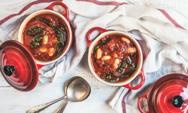 Due ciotole rosse con zuppa di cavolo nero, fagioli e pomodoro, pronte per essere gustate.