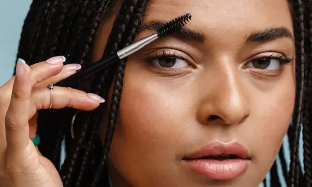 Une femme utilise une brosse pour coiffer son sourcil. La repousse d'un sourcil est une question de patience.