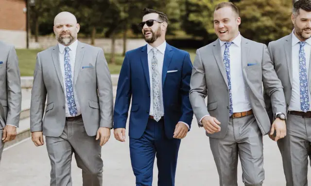 Groomsmen in grey suits and patterned ties walk together, showcasing stylish wedding pocket square folds.