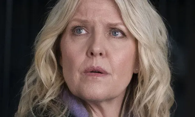 En kvinna med blont hår och blå ögon, klädd i lila, ser oroligt ut. Kanske är hon mitt i ett dramatiskt ögonblick i **shetland serie**.