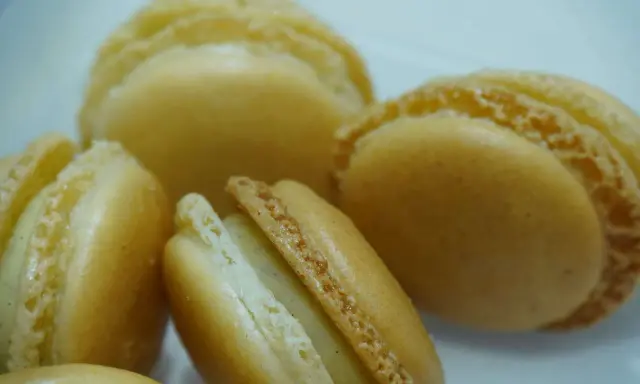 Macarons dorés à la ganache vanille, leurs coques délicates révèlent une garniture crémeuse et parfumée.