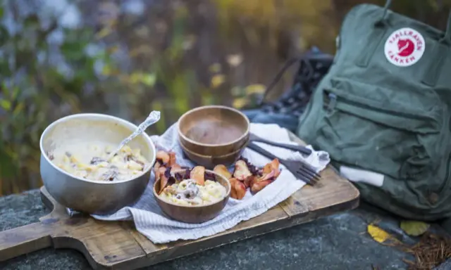 En härlig måltid med pasta och svamp, perfekt för att torka kyckling och njuta av naturen. En Fjällräven ryggsäck och vandringskängor syns i bakgrunden.
