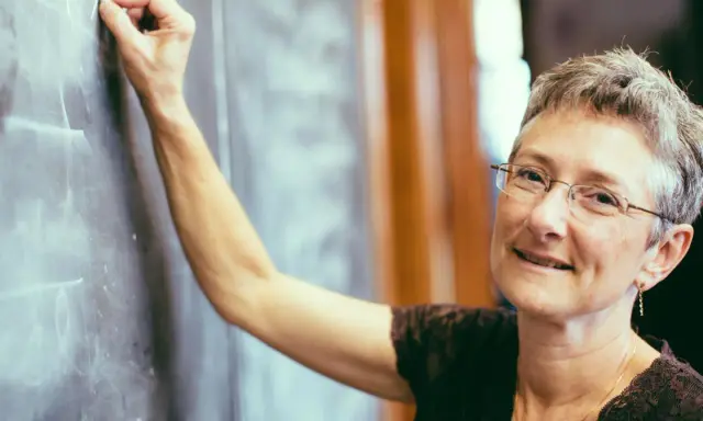 Lehrerin schreibt an Tafel. Was verdient ein Gymnasiallehrer? Sie lächelt wissend.