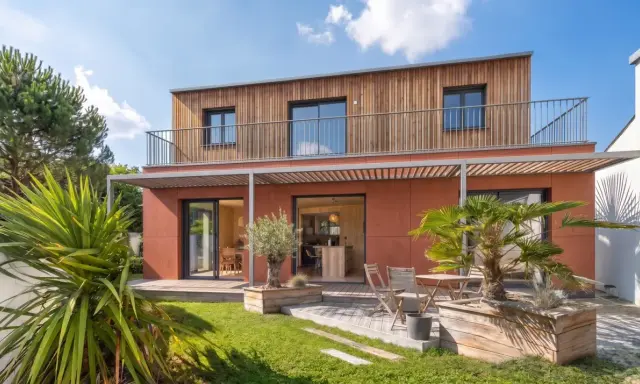 Maison moderne avec bardage bois et façade ocre. Idéal pour un conseil construction maison, avec jardin verdoyant et terrasse accueillante.