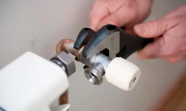 Manos ajustando llave de radiador con llave inglesa para cambiarla y evitar goteos.
