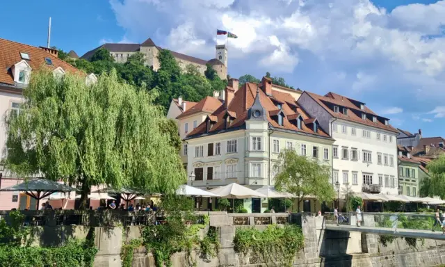 Urokliwy widok na rzekę i zabytkowe kamienice w Słowenii, Lublana. W tle widać zamek na wzgórzu.