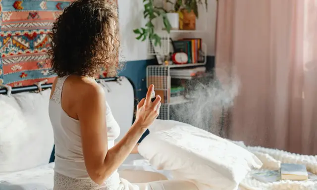 Mujer rocía almohada con spray para eliminar el olor fétido en una habitación.