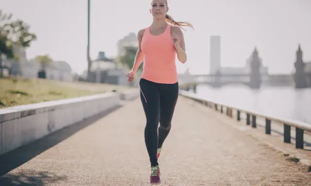 Frau joggt am Fluss entlang. Sie beweist, dass ist joggen gesund und ein toller Start in den Tag.