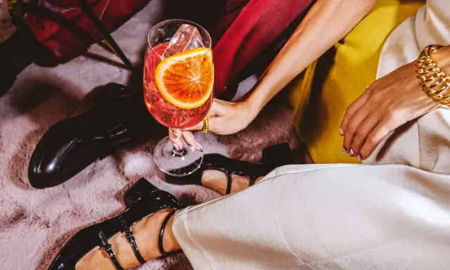 Elegancka kobieta z drinkiem, w którym widać plaster pomarańczy i lód. Zastanawiasz się, wermut co to? To aromatyzowane wino, idealne na letnie wieczory.