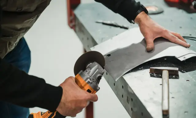 Mężczyzna używa szlifierki kątowej, by ciąć blachodachówkę. Narzędzie to idealnie nadaje się do precyzyjnego cięcia materiałów budowlanych.