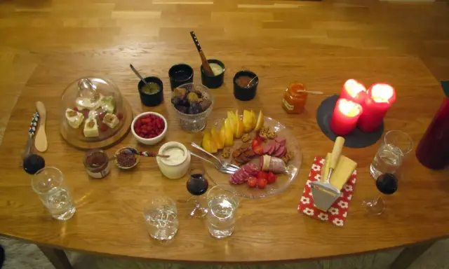 En härlig ostbricka jul med godsaker som frukt, nötter, korv och marmelad. Tre röda ljus lyser upp bordet.