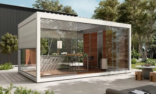 Moderna cucina esterna con tettoia in vetro, completa di bancone, sgabelli e un'elegante lampada da terra.