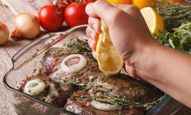 Fleisch marinieren für den Grill: Zitrone über mariniertes Fleisch mit Zwiebeln und Kräutern ausdrücken.