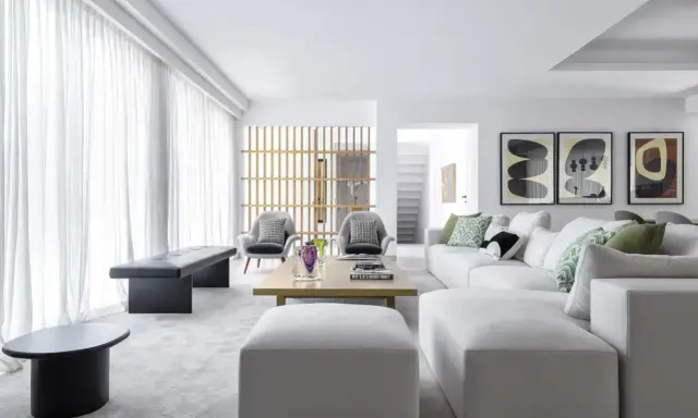 Elegante salón moderno. Sofá blanco modular, butacas grises y mesa de centro de madera. Combinar color gris en salón con toques verdes y arte abstracto.