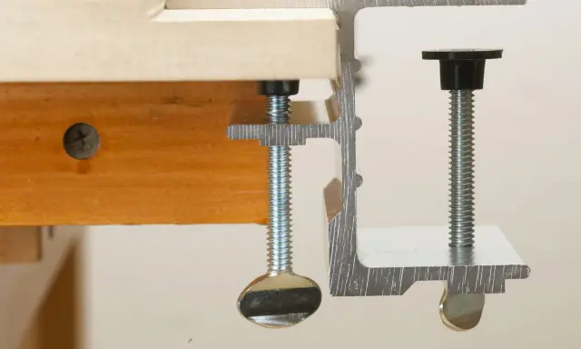 Dos tipos de abrazaderas metálicas sujetan una tabla de madera.