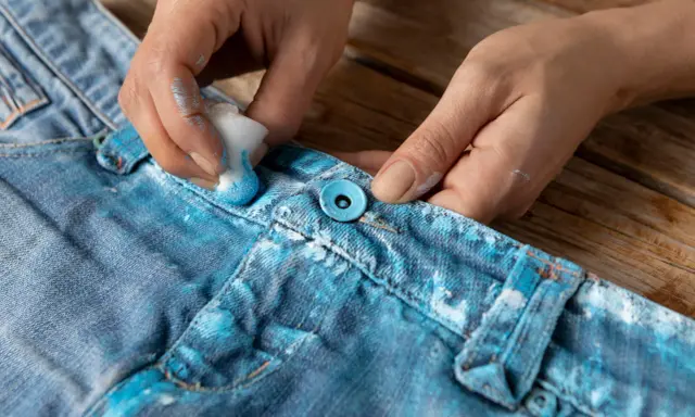 Ręce malują dżinsy na niebiesko, pokazując, jak zafarbować ubranie domowym sposobem. Efekt ombre na materiale.