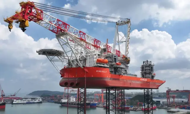 Le bateau grue "Wind Ally" est prêt à installer une éolienne en mer. Sa structure imposante domine le port.