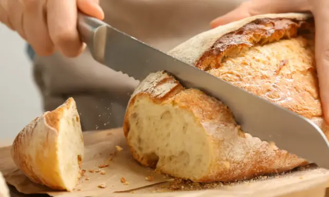 Krojenie świeżo upieczonego bochenka, idealnego na domowy przepis na chleb pieczony w piekarniku. Chrupiąca skórka i miękki środek.