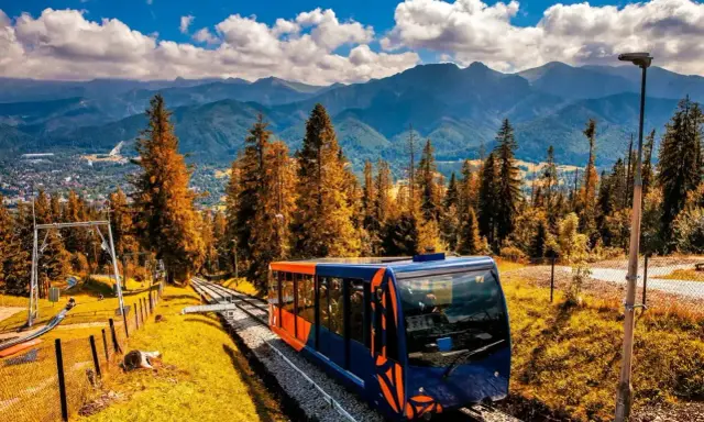 Kolejka linowo-terenowa na Gubałówkę, z widokiem na Tatry. Jesienne kolory drzew i błękitne niebo. Wejście pieszo na Gubałówkę to wspaniała przygoda.