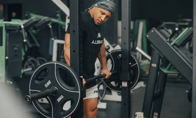 Mann im Fitnessstudio bereitet sich auf schwere myo reps vor, hält eine Langhantel mit 20kg Scheiben.