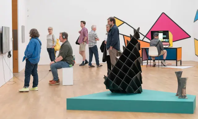 Visitors explore diverse artworks in what is an art gallery, from video installations to abstract sculptures and colorful wall art.