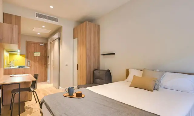 Habitación moderna con cama, escritorio y cocina. Descubre los livensa living precios para tu estancia.
