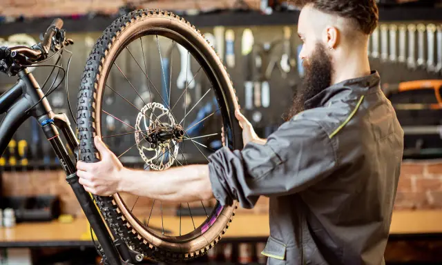 Mechanik z brodą sprawdza oponę gravelową roweru. Zastanawia się, ile mleka do opony gravel będzie potrzebne, by zapewnić najlepszą przyczepność.