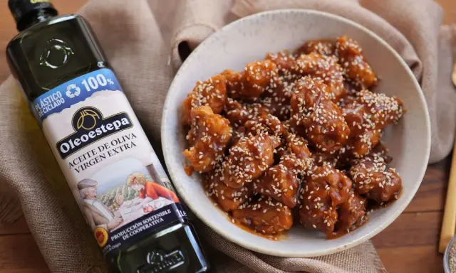 Delicioso pollo agridulce cubierto de semillas de sésamo en un cuenco, junto a una botella de aceite de oliva virgen extra Oleoestepa.