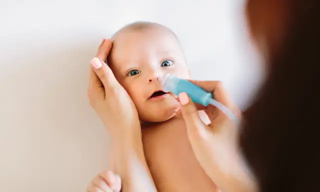 Mama delikatnie oczyszcza nosek niemowlaka z katarem za pomocą aspiratora.