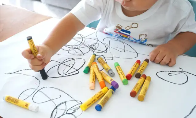 Bambino disegna con pastelli su foglio bianco. I disegni dei bambini sono un modo per esprimere emozioni, ma quando preoccuparsi?