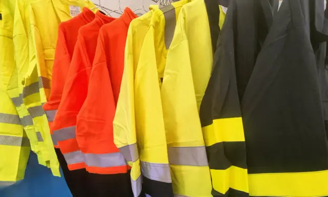 Variedad de ropa de alta visibilidad normativa en colores amarillo, naranja y negro, con bandas reflectantes para garantizar la seguridad en entornos de trabajo.