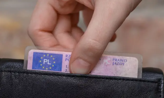 Dłoń wyjmuje z czarnego portfela polskie prawo jazdy.