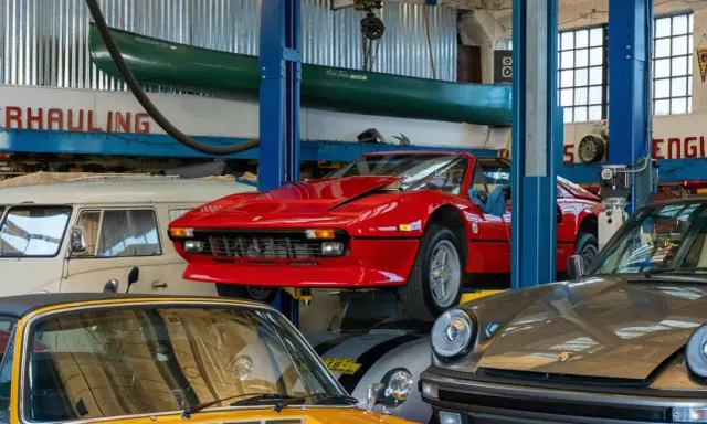 Taller mecánico con autos clásicos: un rojo Ferrari en elevador, un Porsche gris y un amarillo. ¡Ideas para tu taller!