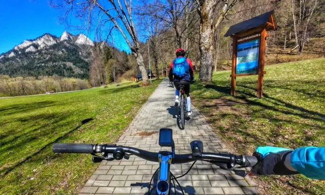 Rowerzyści przemierzają malowniczą ścieżkę rowerową w Szczawnicy, podziwiając górskie krajobrazy.