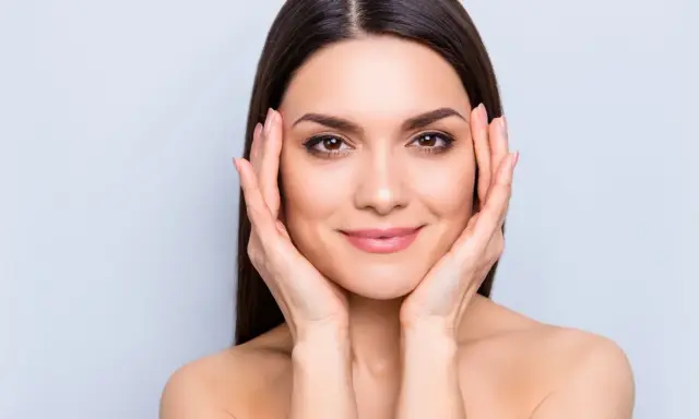 Mujer con piel radiante, resultado del colágeno para la piel. Sus manos acarician su rostro, mostrando una tez suave y luminosa.