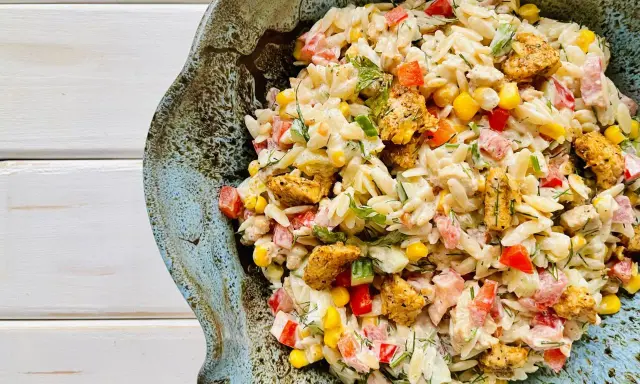 Pyszna sałatka z makaronem orzo i kurczakiem, z dodatkiem kukurydzy, papryki i ziół, podana w ceramicznej misie.