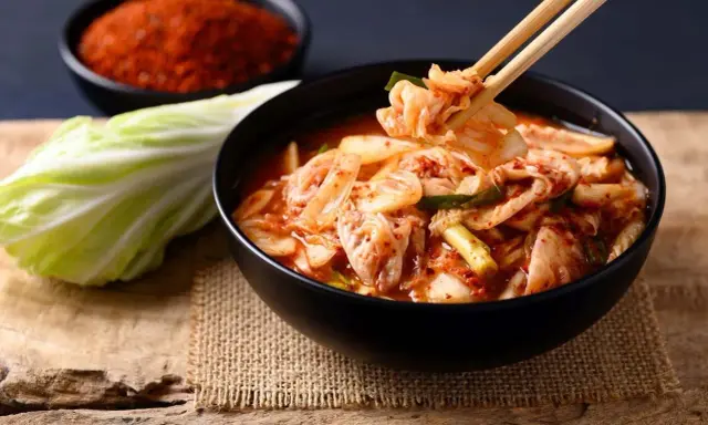 Miseczka z kimchi, pałeczki podnoszące kawałek kapusty, obok kapusta i miseczka z przyprawą.