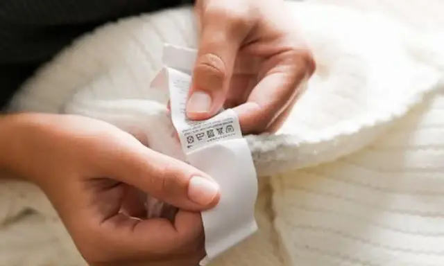 Dłonie trzymają białą metkę z symbolami pielęgnacji. To oryginalna metka Off-White, która informuje o sposobie prania swetra.