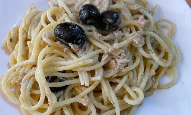 Un piatto di spaghetti conditi con tonno e olive nere, un classico della cucina italiana.