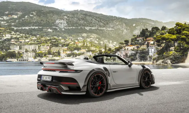 Ein weißer Techart GTstreet RS Cabriolet steht an einer Küstenstraße mit Blick auf eine malerische Stadt am Hang.
