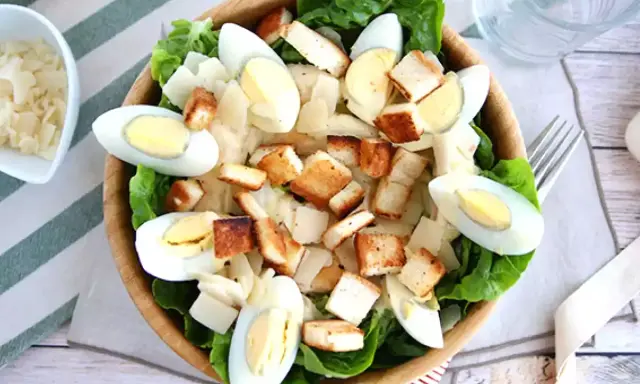 Salade César maison appétissante avec laitue, œufs durs, croûtons dorés et copeaux de parmesan. Parfait pour une recette facile et savoureuse.