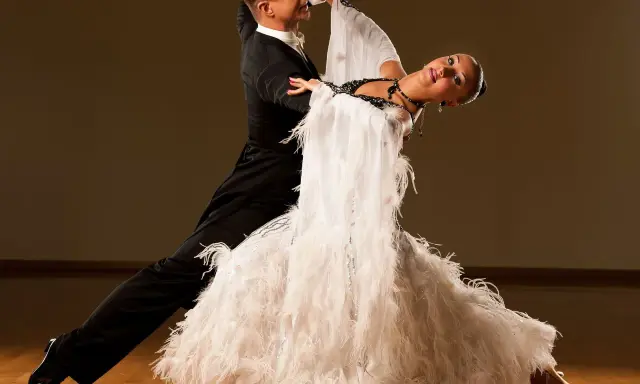Elegancka para tańczy walca wiedeńskiego. Mężczyzna w czarnym fraku, kobieta w białej sukni z piórami. Ich ruchy to perfekcyjne walc wiedeński kroki.