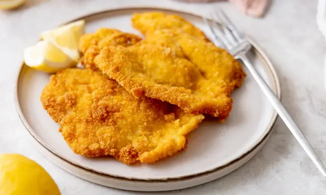Piatto di cotolette di pollo dorate e croccanti, servite con spicchi di limone fresco e una forchetta.