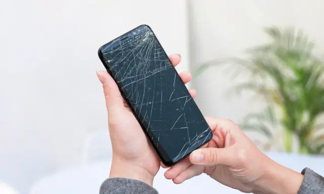 Dłoń trzyma pęknięty telefon, czekając na wymianę ekranu.